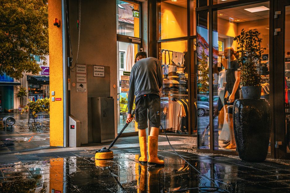 A professional cleaning team from Bayswater Carpet Cleaners is performing surface cleaning and deep cleaning in a modern living room with wooden flooring. The room features a large, L-shaped fabric so